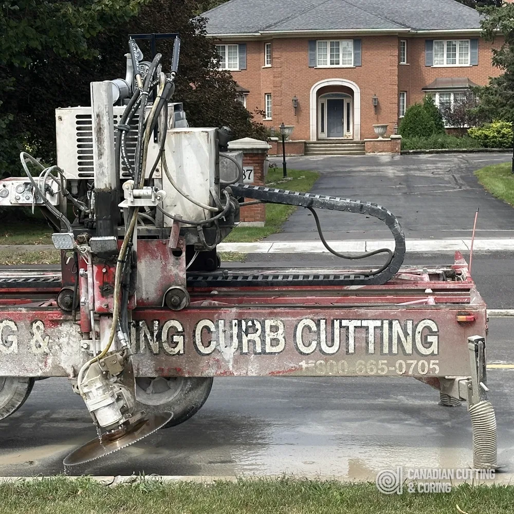 Canadian Cutting & Coring tow-behind curb saw cutting a residential curb in front of a brick house