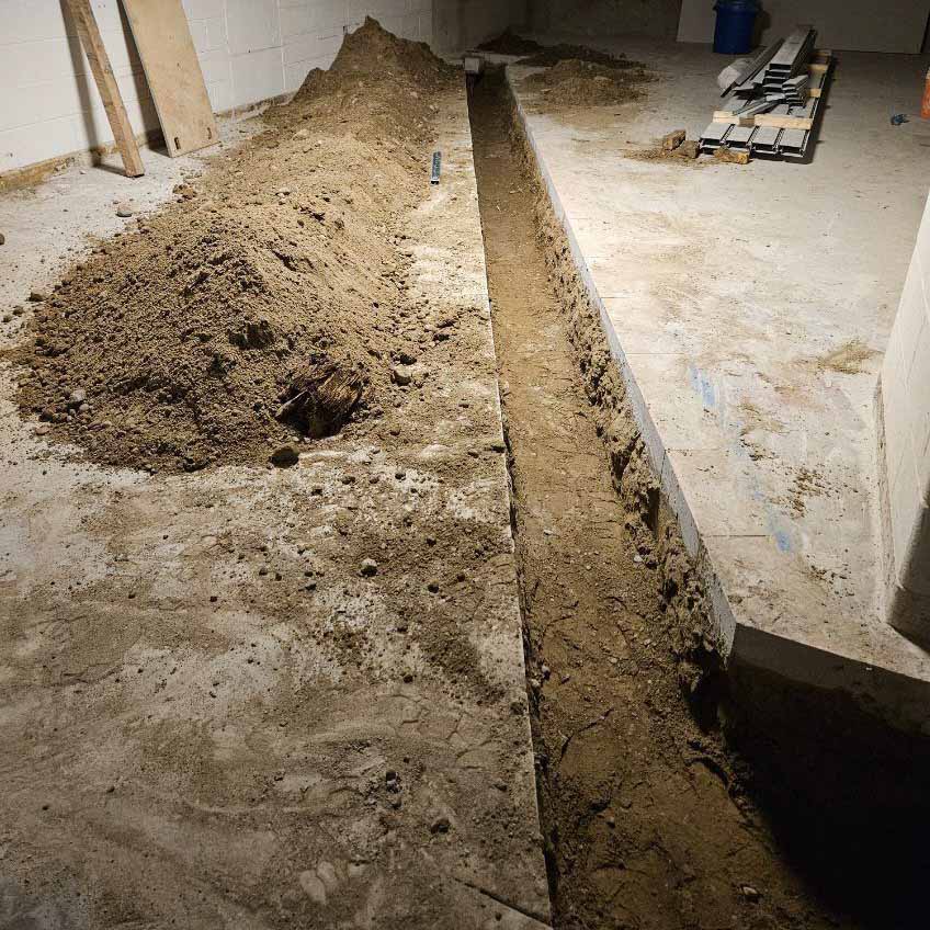 Electric mini excavator digging a utility trench through a concrete floor inside a building