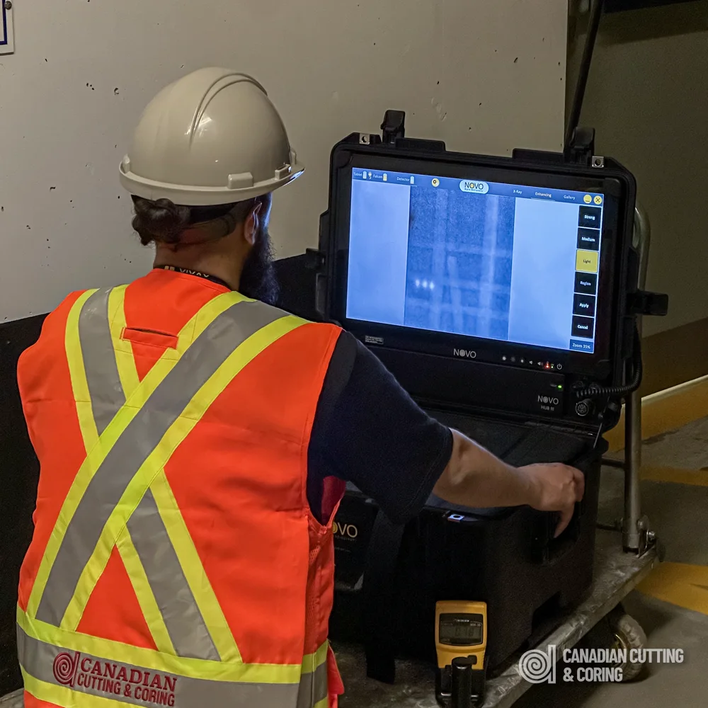 Radiography technician at the digital X-ray unit reading a live radiograph of a concrete slab on site